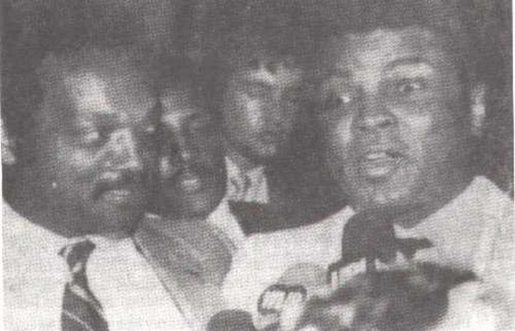 A 1984 image of Jesse Jackson and Muhammad Ali. A person resembling Elvis Presley can be seen in the background.