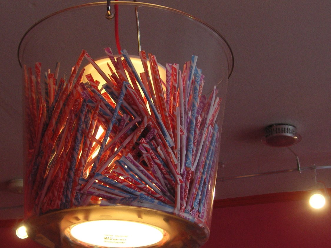 Dozens of thin Pixy Stix candy straws packed into a clear bucket lamp hanging from a ceiling