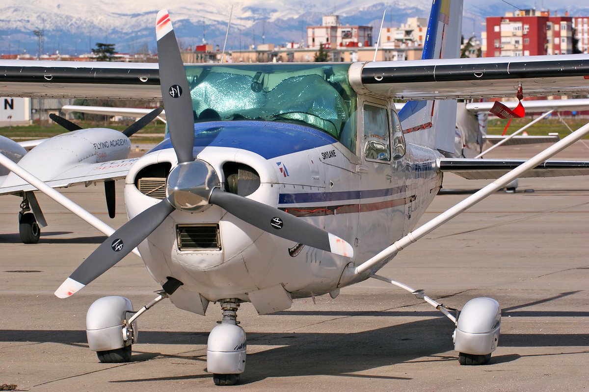 A white and blue Cessna 182L Skylane single-engine light aircraft parked on an airfield apron